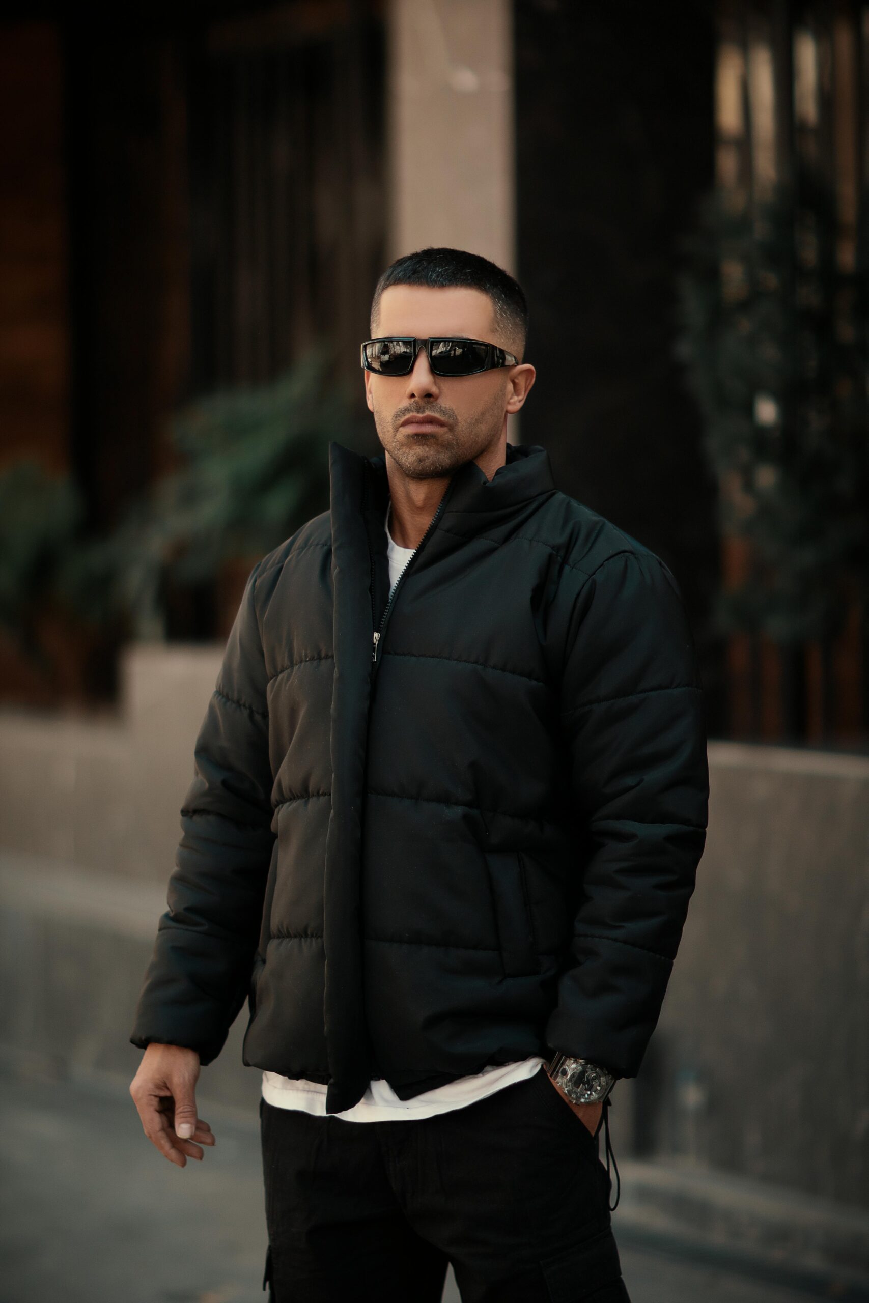 A fashionable man outdoors wearing sunglasses and a jacket, exuding urban style and confidence.